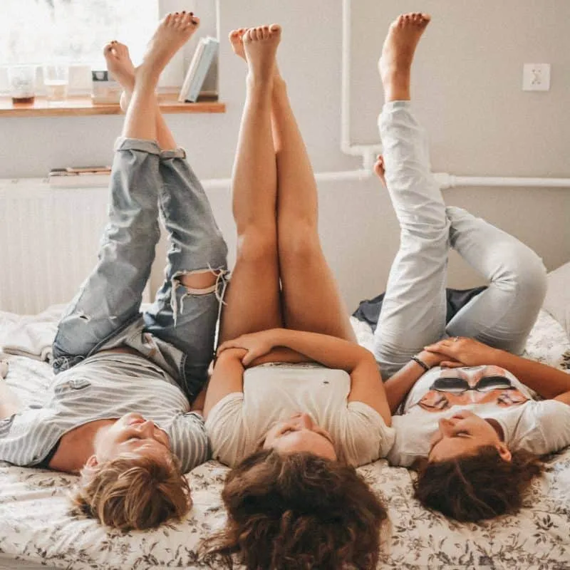 3 friends lying on a bed with their feet up in the air