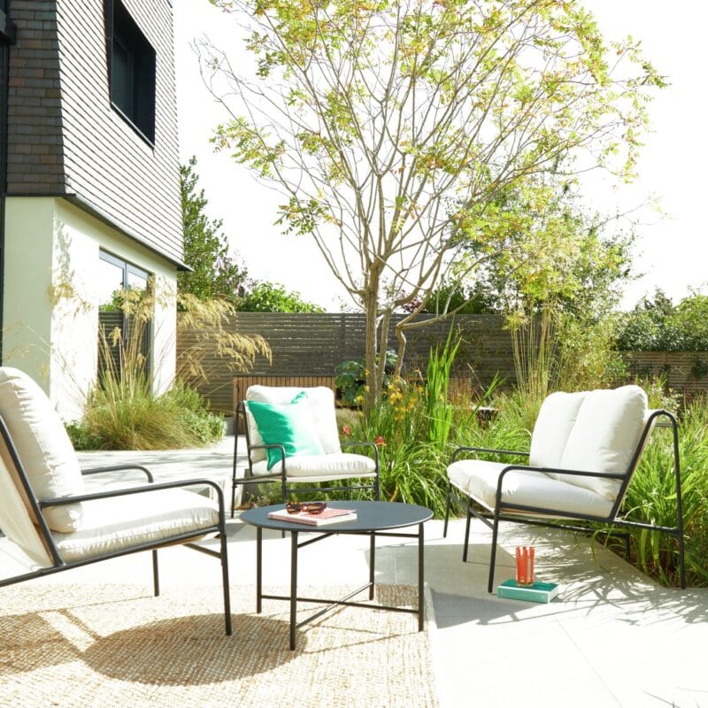 Garden sofa and two matching chairs with a slender black metal frame and cream coloured cushions plus a round black metal coffee table